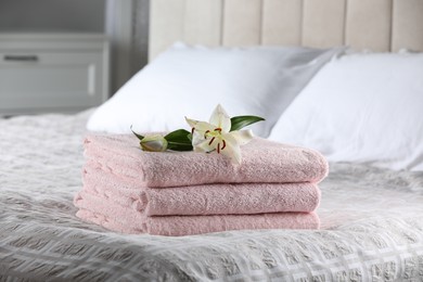 Photo of Stack of clean towels and lily flowers on bed indoors