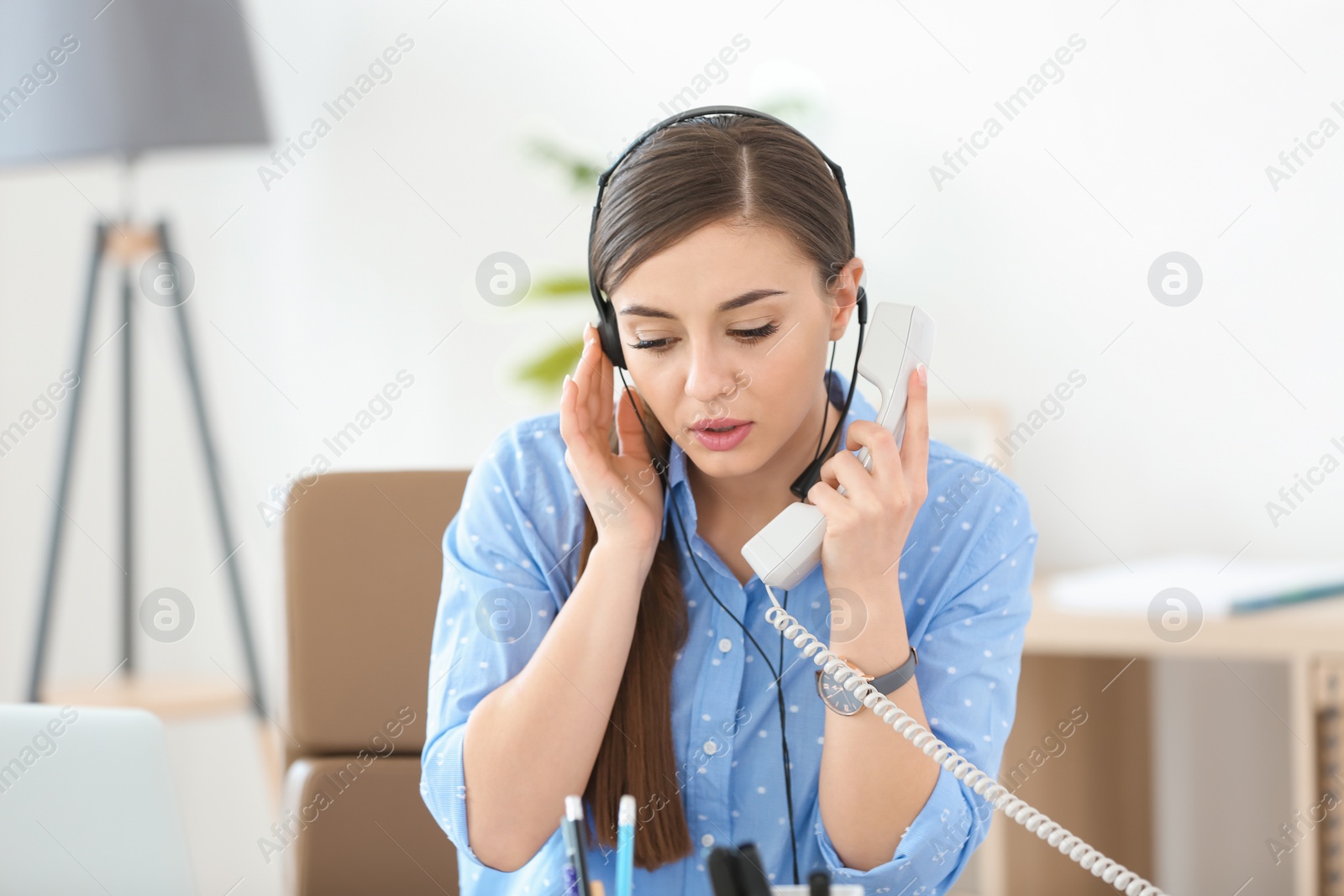 Photo of Young woman talking on phone through headset at workplace