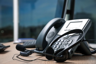 Photo of Stationary phone and headset on wooden desk indoors, closeup. Hotline service
