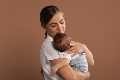 Mother holding her cute newborn baby on brown background