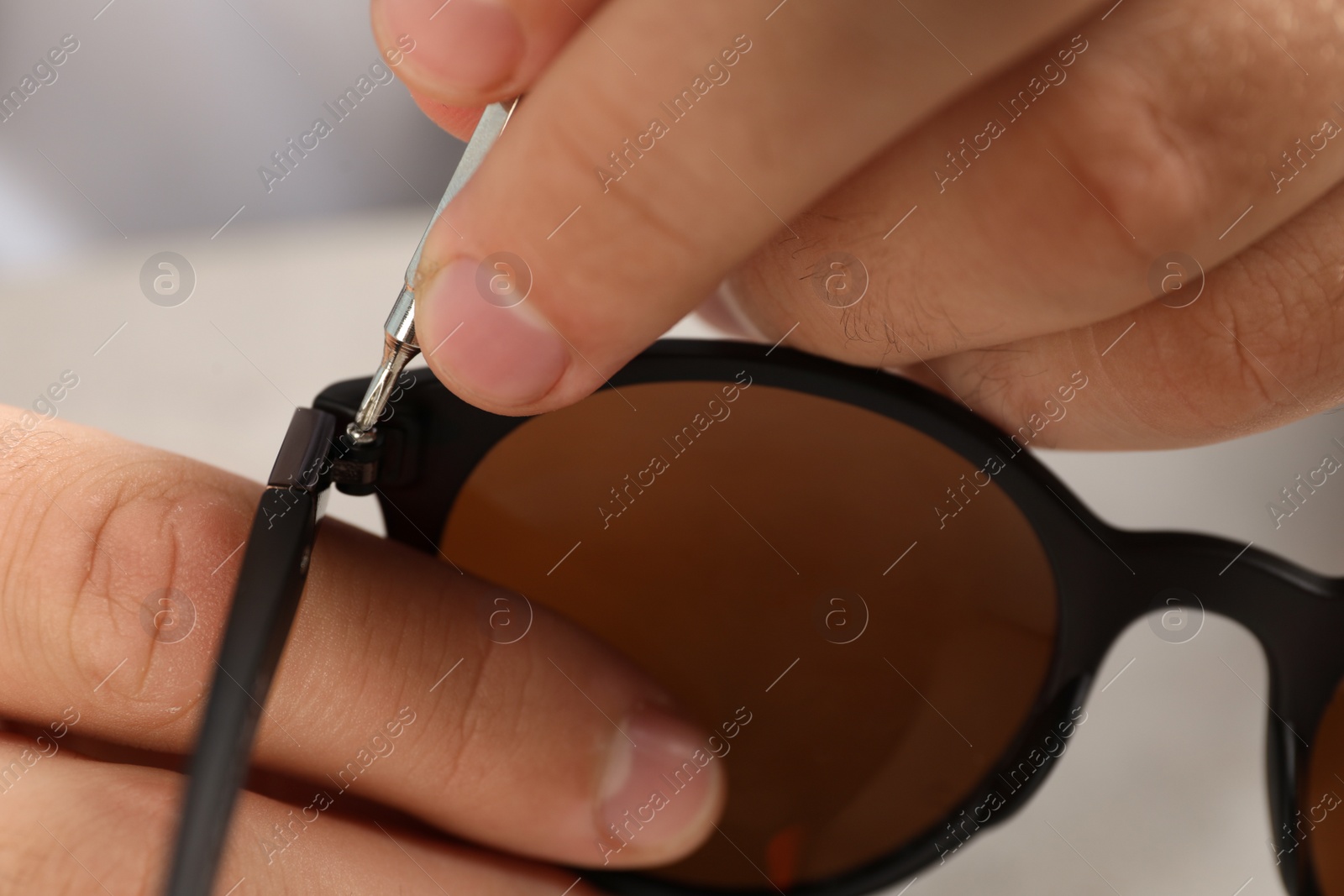 Photo of Handyman repairing sunglasses with screwdriver at grey table, closeup