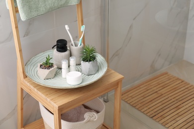 Photo of Holder with toothbrushes, different toiletries and plants on wooden rack in bathroom. Space for text