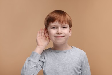 Little boy with hearing problem on pale brown background