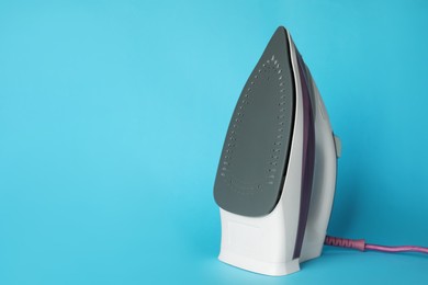 Photo of One modern iron on light blue background, space for text. Home appliance