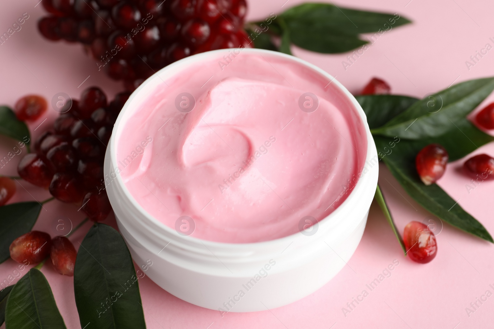 Photo of Fresh pomegranate and jar of facial mask on pink background, closeup. Natural organic cosmetics