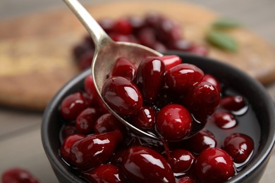 Photo of Spoon with delicious dogwood jam and berries over bowl, closeup