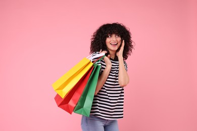 Happy young woman with shopping bags on pink background