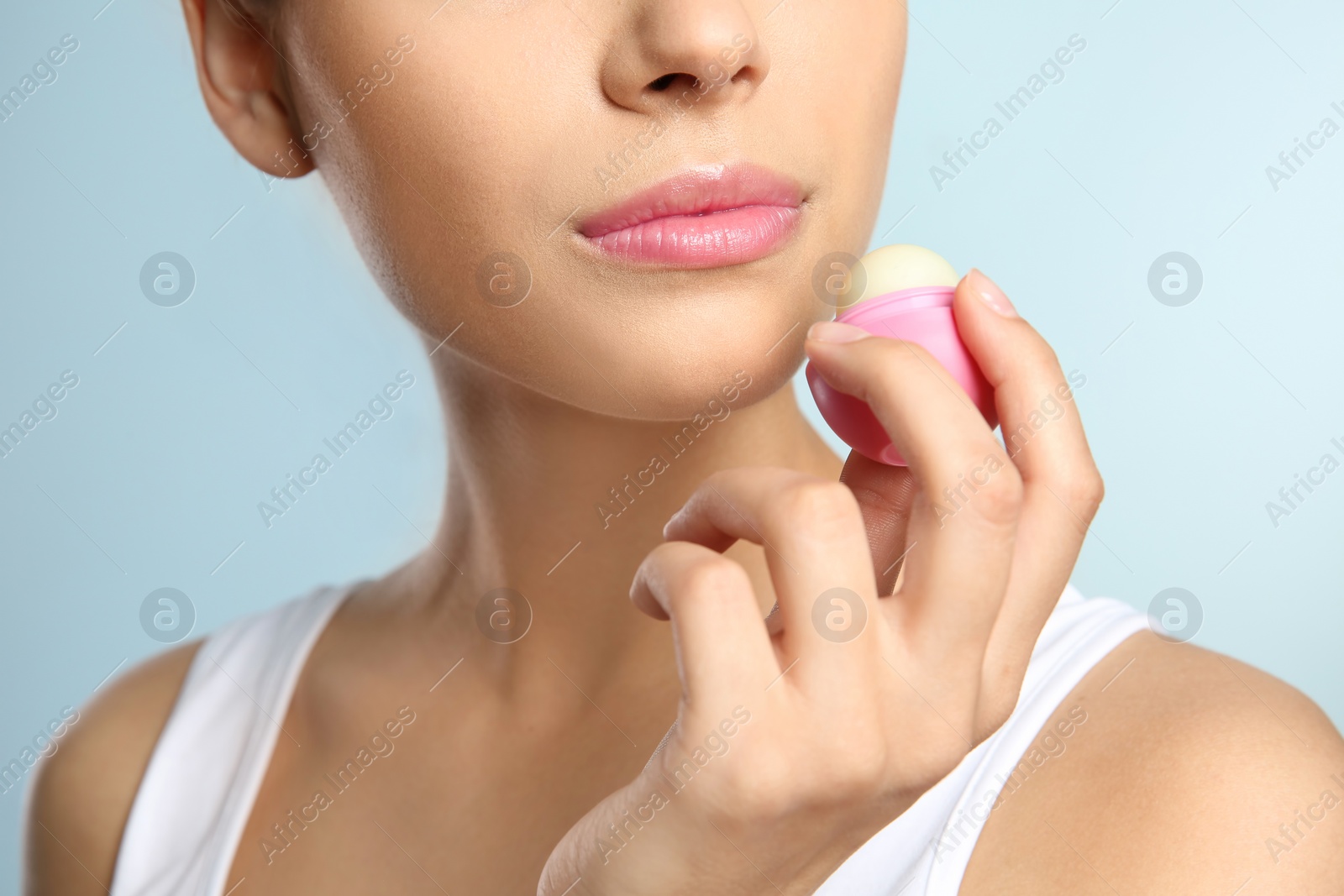 Photo of Young woman applying balm on her lips against color background, closeup