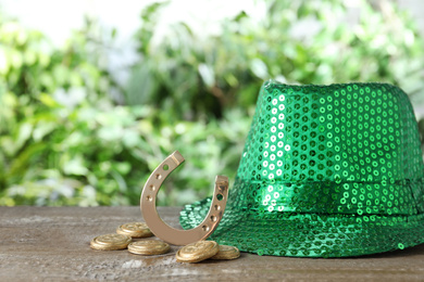 Photo of Green leprechaun hat, horseshoe and gold coins on wooden table, space for text. St Patrick's Day celebration
