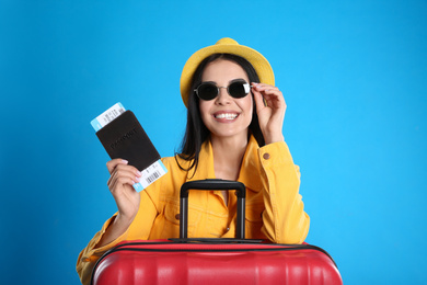 Beautiful woman with suitcase and ticket in passport for summer trip on blue background. Vacation travel