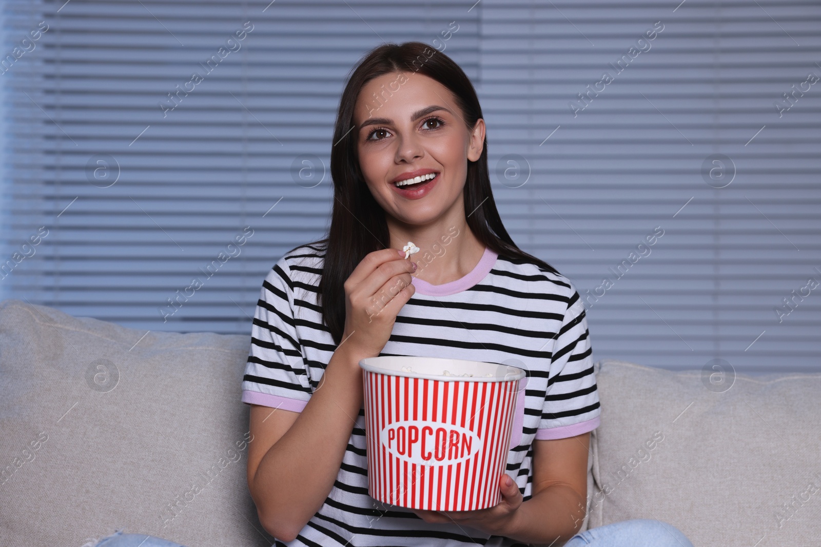 Photo of Happy woman eating popcorn while watching TV at home in evening