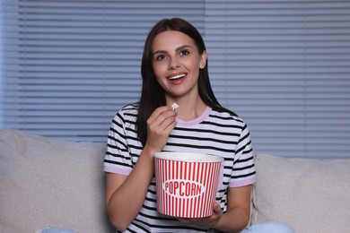Photo of Happy woman eating popcorn while watching TV at home in evening