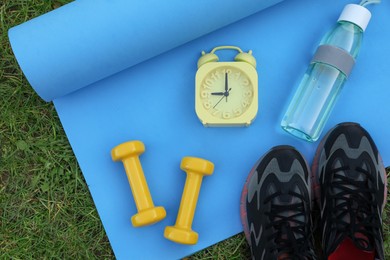 Photo of Alarm clock and morning exercise set on green grass, flat lay