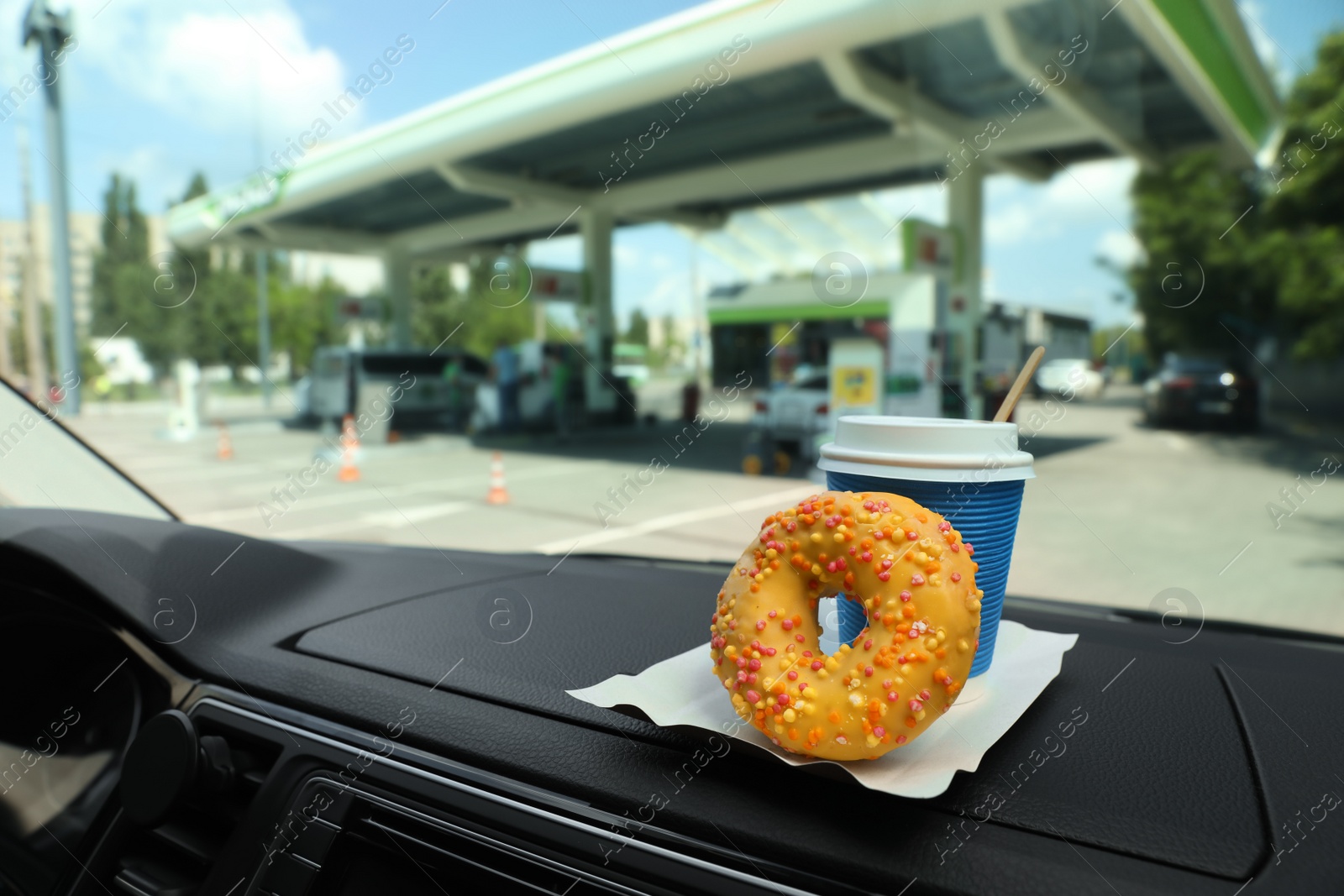 Photo of Paper coffee cup and doughnut on car dashboard at gas station