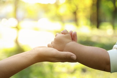 Daughter holding mother's hand outdoors, closeup. Happy family
