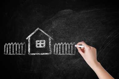 Image of Woman drawing house with fence on chalkboard, closeup