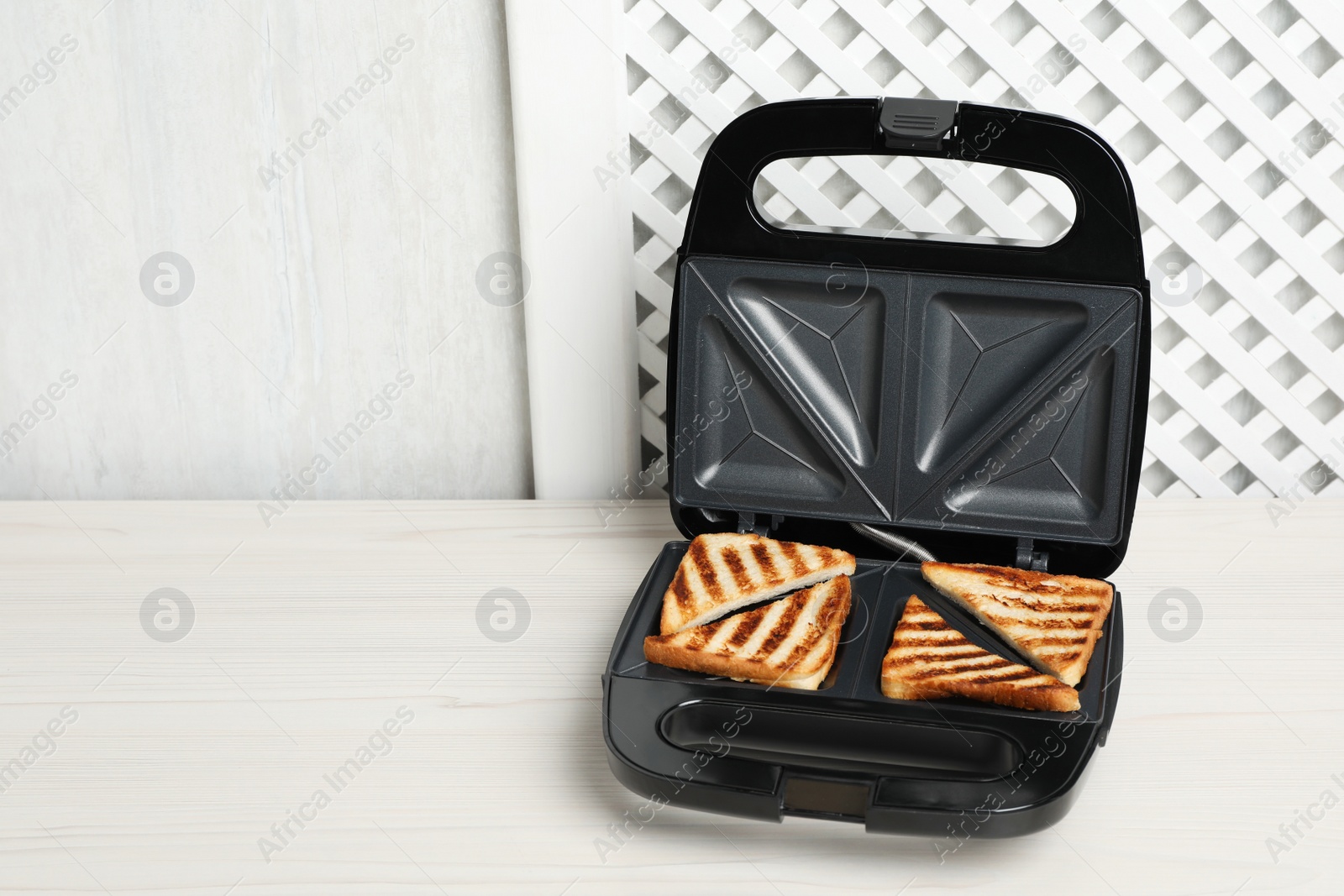 Photo of Modern sandwich maker with bread slices on white wooden table, space for text