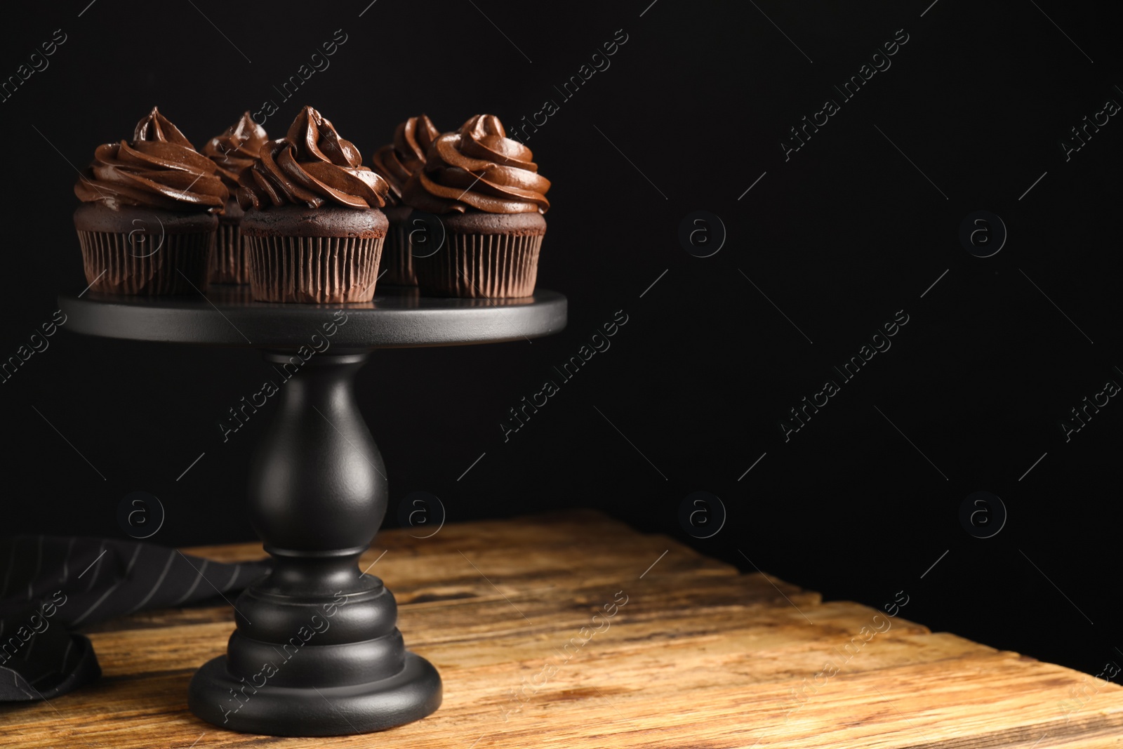 Photo of Dessert stand with delicious chocolate cupcakes on wooden table against black background. Space for text