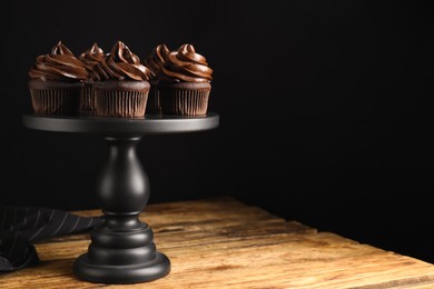 Photo of Dessert stand with delicious chocolate cupcakes on wooden table against black background. Space for text