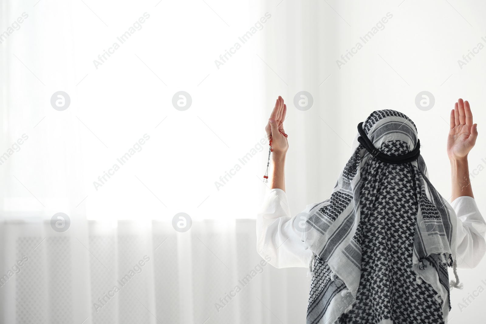 Photo of Muslim man in traditional clothes praying indoors. Space for text