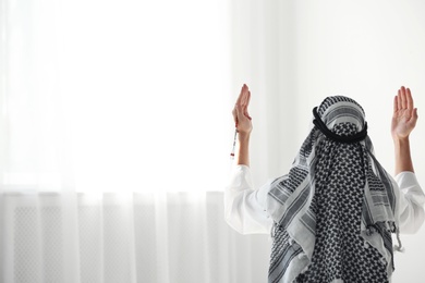 Muslim man in traditional clothes praying indoors. Space for text