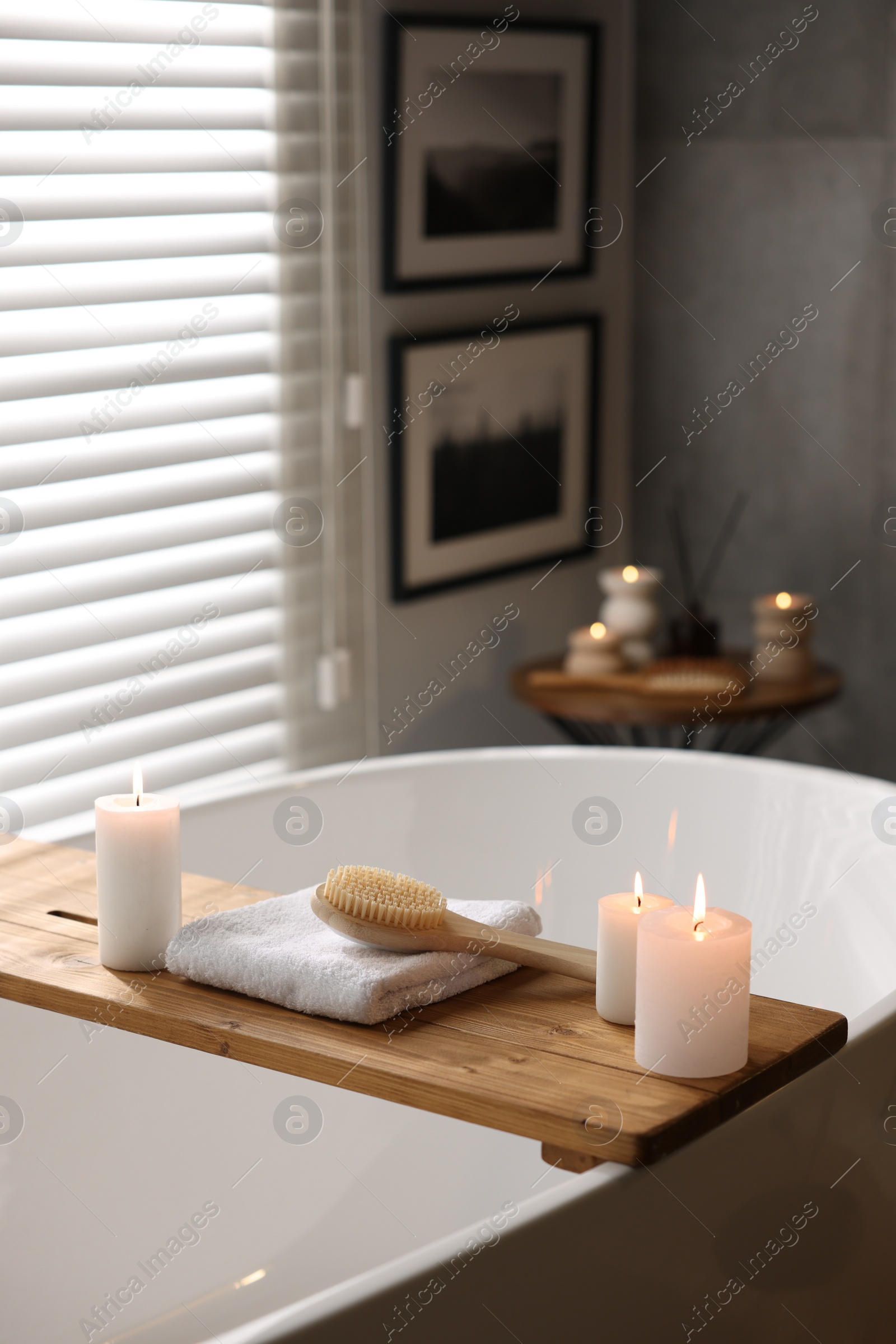 Photo of Wooden tray with burning candles, towel and brush on bathtub in bathroom