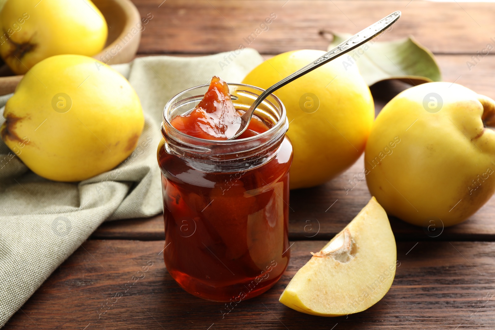 Photo of Tasty homemade quince jam in jar, spoon and fruits on wooden table