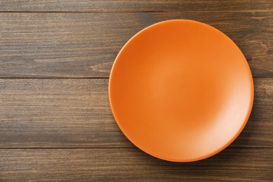 Empty orange ceramic plate on wooden table, top view. Space for text