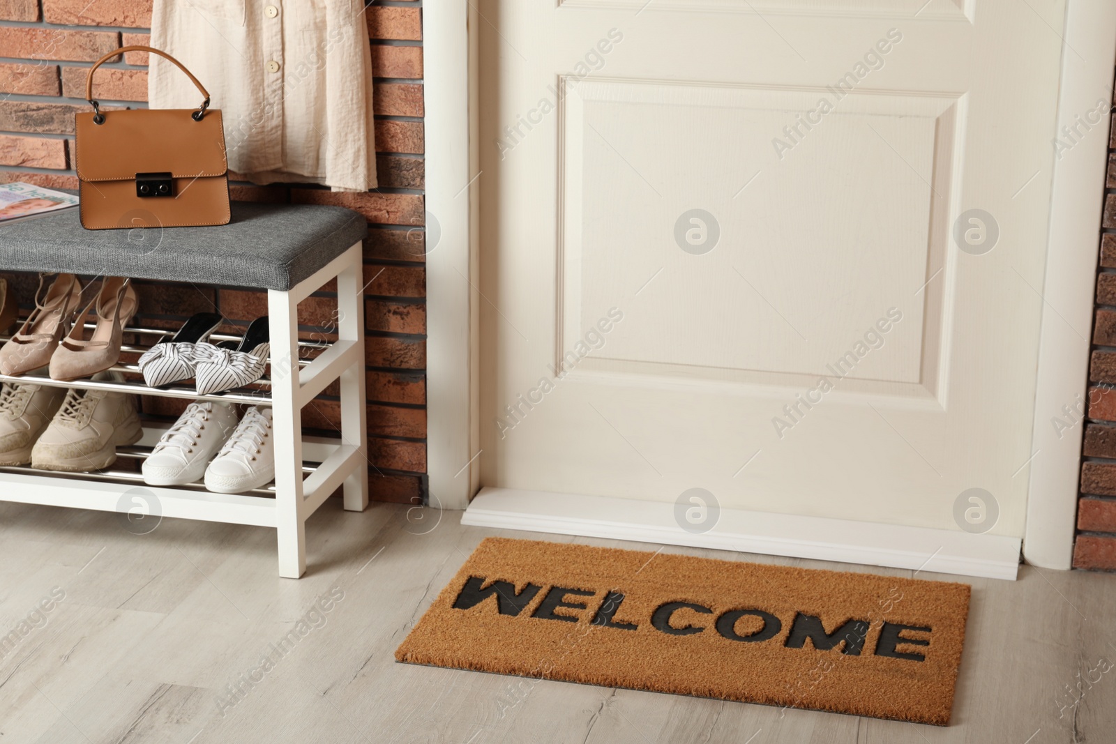 Photo of Doormat with word Welcome near shoe rack on white wooden floor in hall