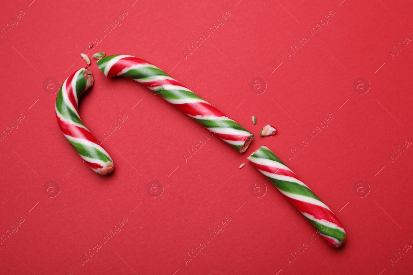 Photo of Broken sweet Christmas candy cane on red background, top view