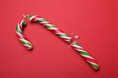 Photo of Broken sweet Christmas candy cane on red background, top view
