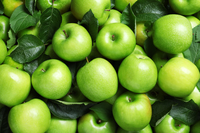 Pile of tasty green apples with leaves as background, top view