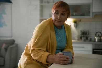 Elderly woman with cup of tea at table in kitchen