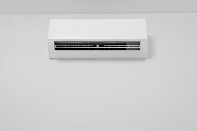 Modern air conditioner on white wall indoors, low angle view. Space for text