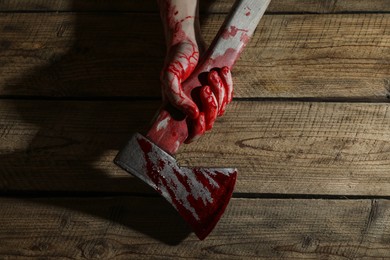 Man holding bloody axe on wooden surface, top view