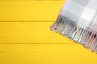 Photo of Soft checkered scarf on yellow wooden table, top view. Space for text