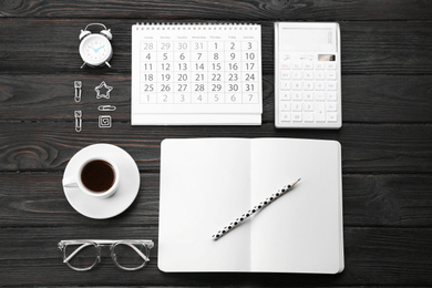 Flat lay composition with calendar and cup of coffee on black wooden table