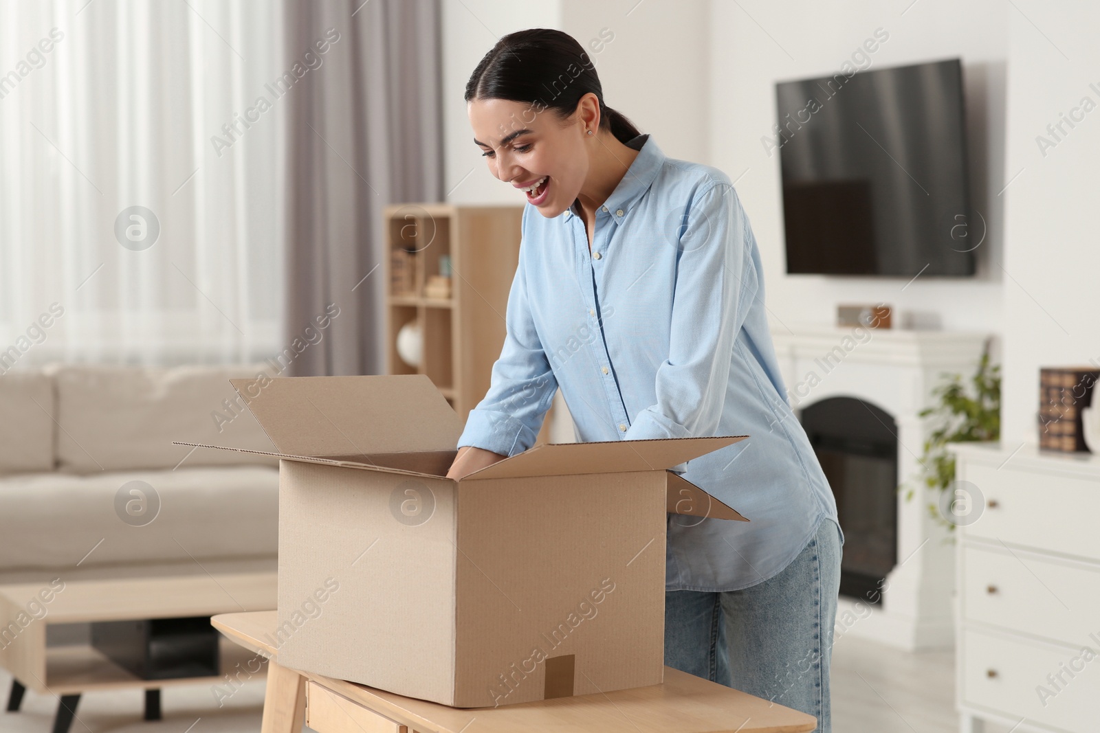 Photo of Happy young woman unpacking parcel at home. Internet shopping