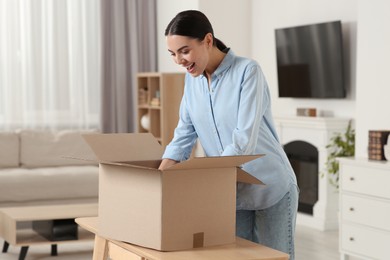 Photo of Happy young woman unpacking parcel at home. Internet shopping