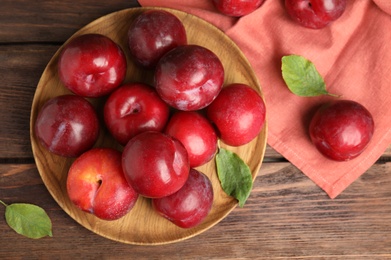 Delicious ripe plums on wooden table, flat lay