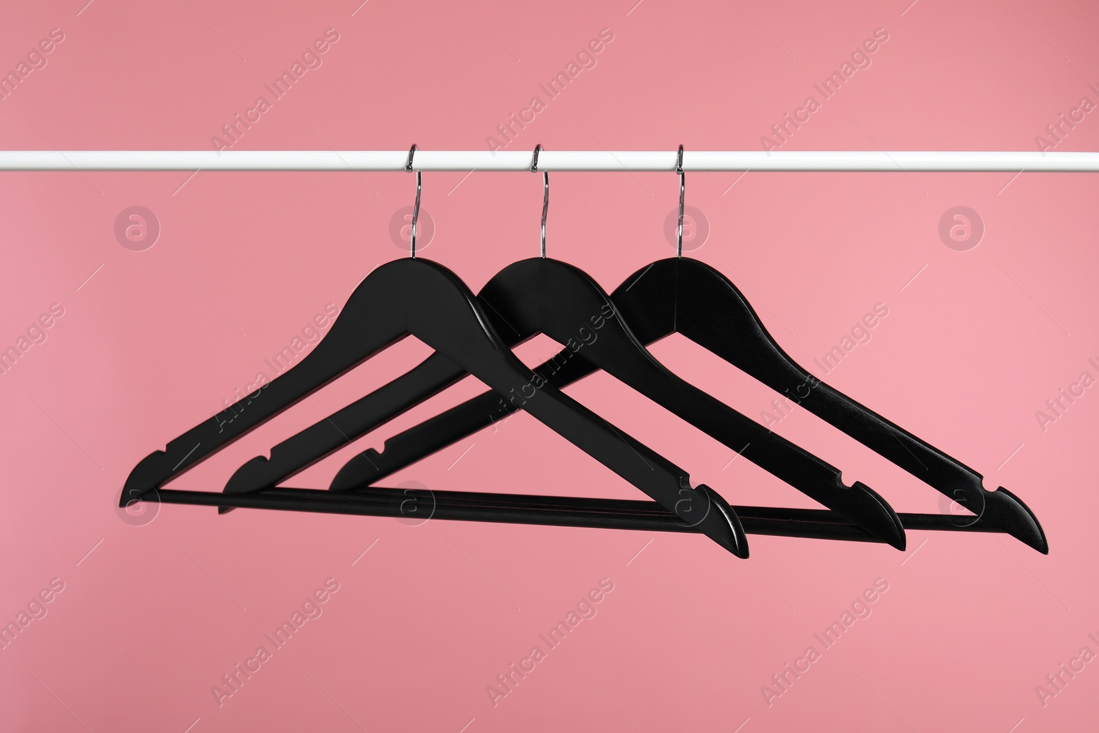 Photo of Black clothes hangers on rack against pink background