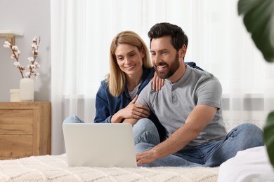 Happy couple with laptop on bed at home
