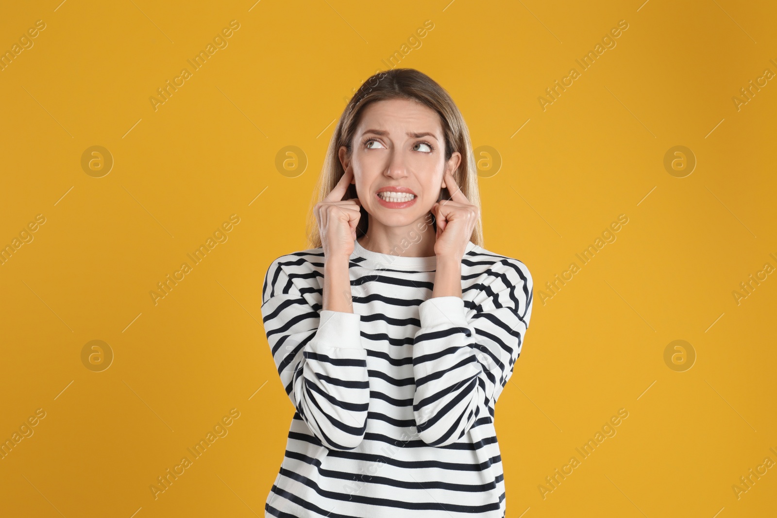 Photo of Emotional young woman covering her ears with fingers on yellow background