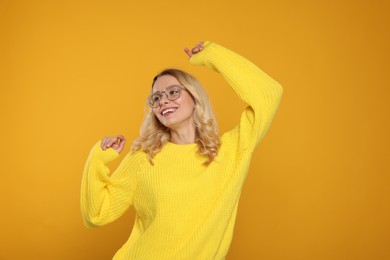 Happy woman in stylish warm sweater and eyeglasses on orange background