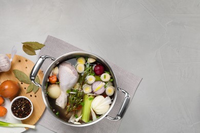 Photo of Pot and different ingredients for cooking tasty bouillon on light grey table, flat lay. Space for text