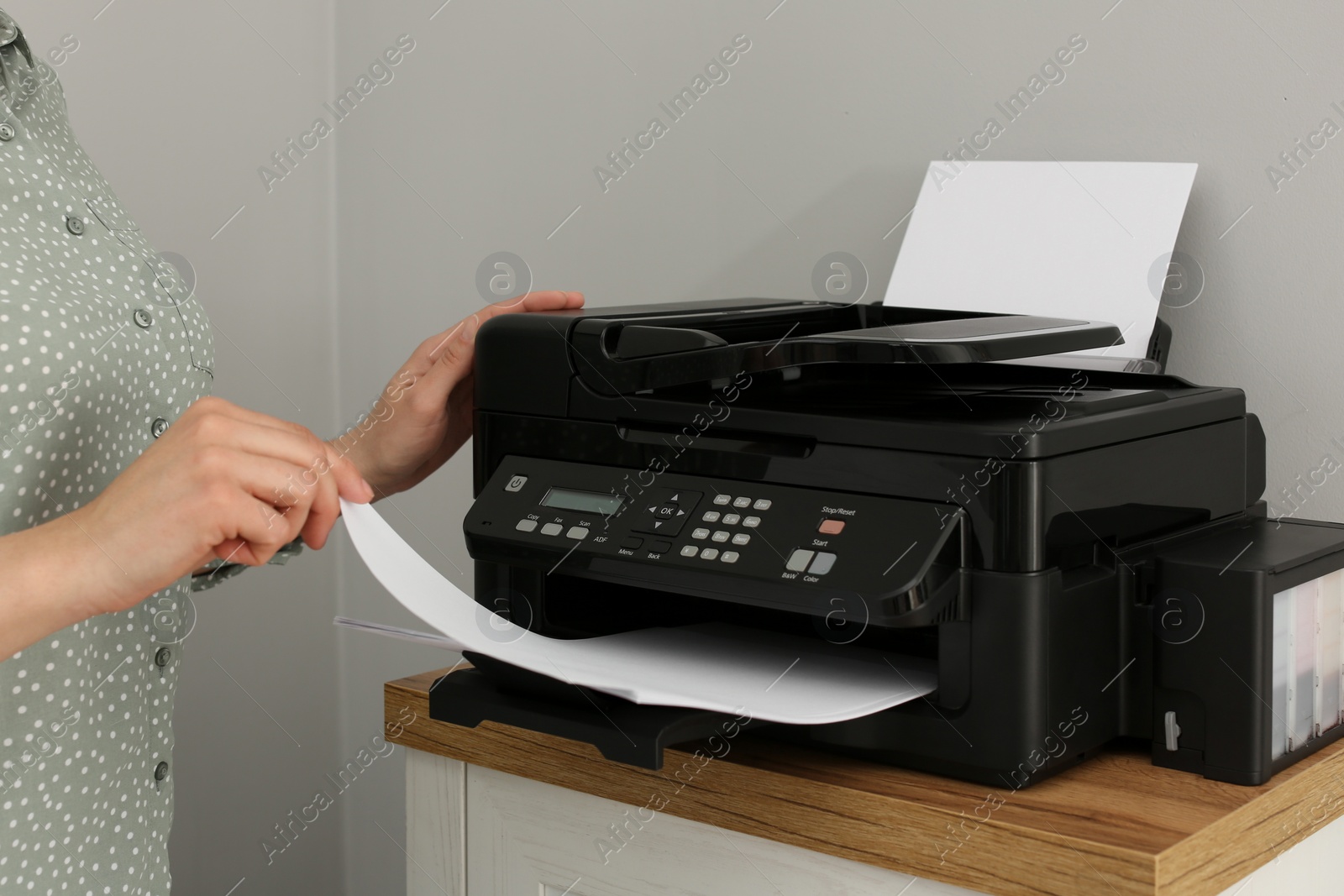 Photo of Woman using modern printer on chest of drawers at home, closeup