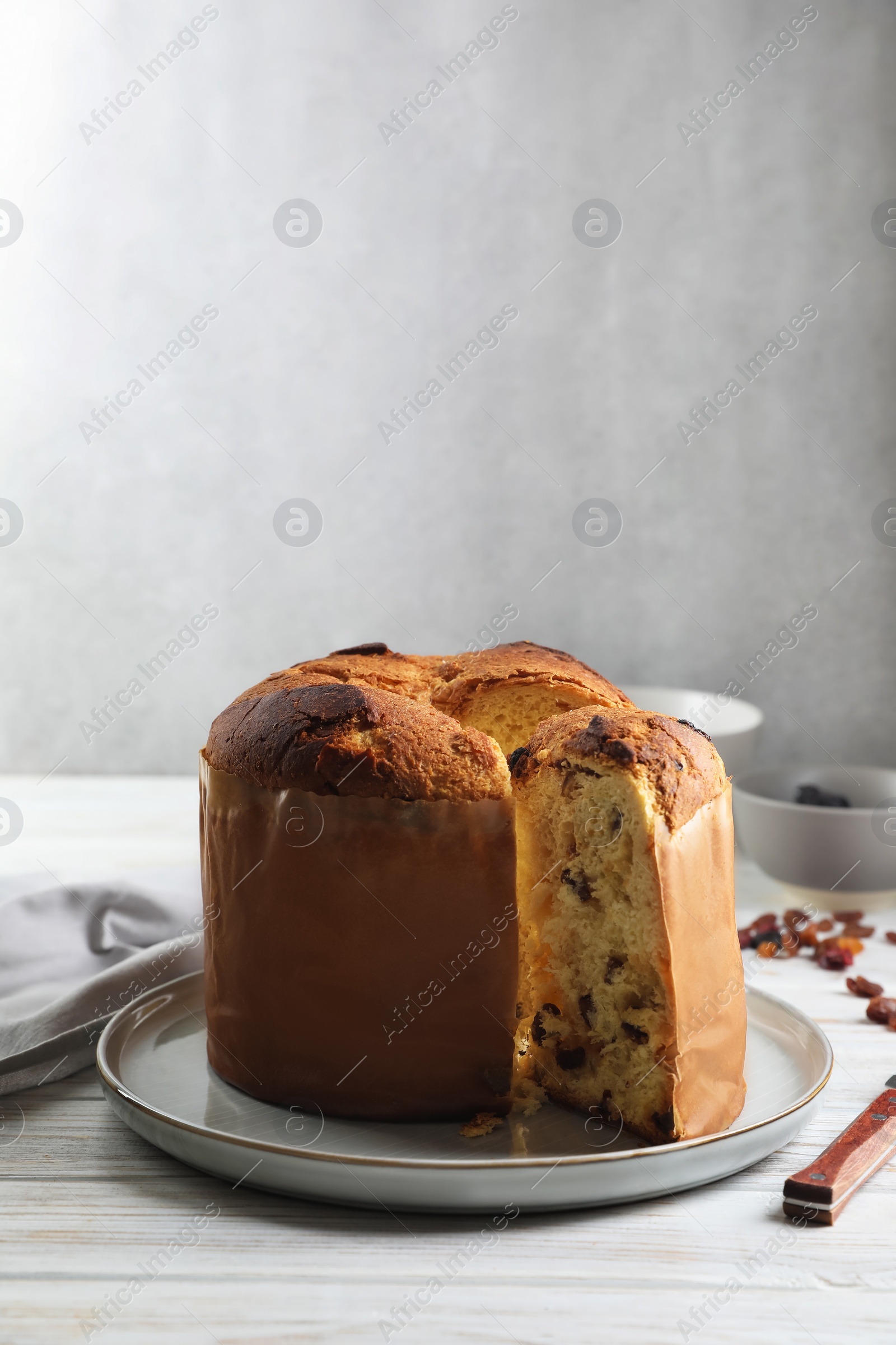 Photo of Delicious cut Panettone cake with raisins on white wooden table. Traditional Italian pastry