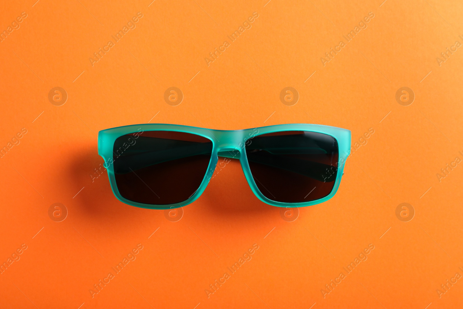 Photo of Stylish sunglasses on orange background, top view