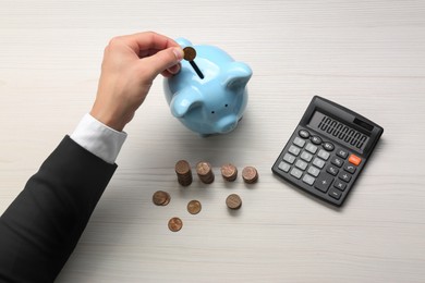 Photo of Budget planning. Businessman putting coin into piggy bank at light wooden table, closeup