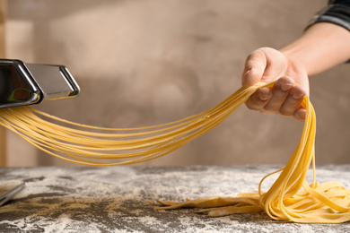 Photo of Woman preparing noodles with pasta maker machine at table, closeup